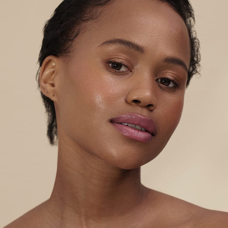 Woman with short curls and deep skin tone wearing Henné Organics Luxury Lip Tint in Azalea 5