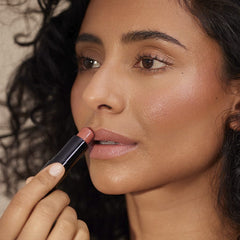 Woman with curly hair applying Henné Organics Luxury Lip Tint in Bare for a sheer rosy nude lip color 4