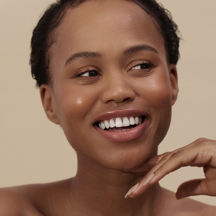 Smiling woman with deep skin tone wearing Henné Organics Luxury Lip Tint in Bare for a sheer nude lip 3