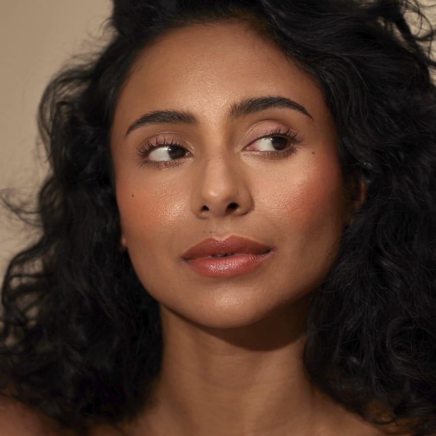 Woman with curly hair wearing Henné Organics Luxury Lip Tint in Coral for a soft peachy coral lip 3