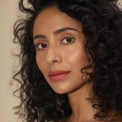 Woman with curly hair wearing Henné Organics Luxury Lip Tint in Desire for a soft coral red lip 3