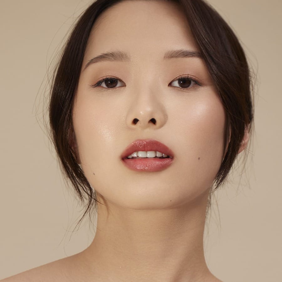 Model wearing Henné Organics Luxury Lip Tint in Desire for glossy hydrated lips with sheer red color 2