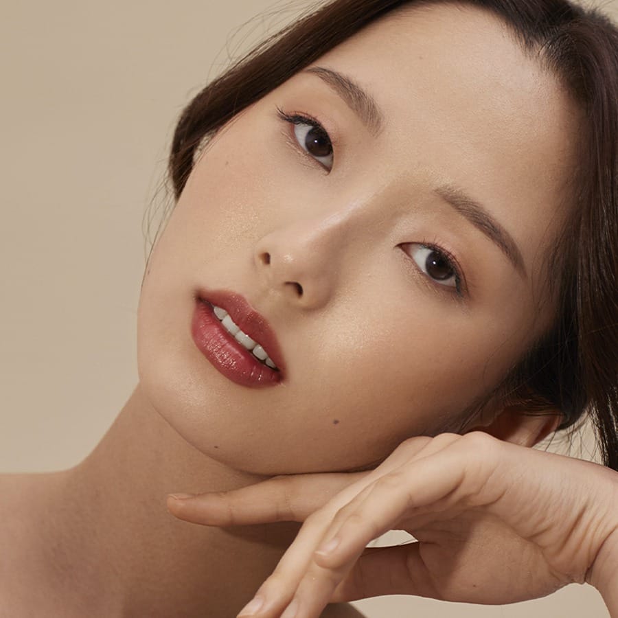 Model resting her chin on her hand wearing Henné Organics Luxury Lip Tint in Intrigue for a glossy red lip 2