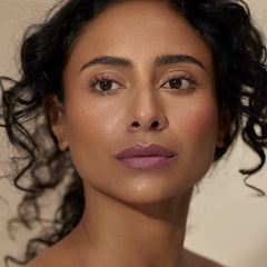 Woman with curly hair wearing Henné Organics Luxury Lip Tint in Muse for a soft mauve plum lip 2