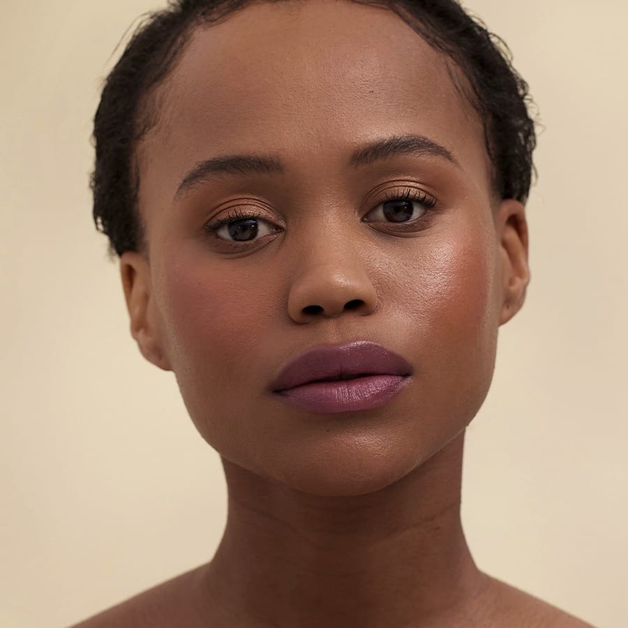 Woman with short curls and deep skin tone wearing Henné Organics Luxury Lip Tint in Muse 4
