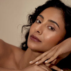 Woman with curly hair resting on her hands wearing Henné Organics Luxury Lip Tint in Nightfall 2