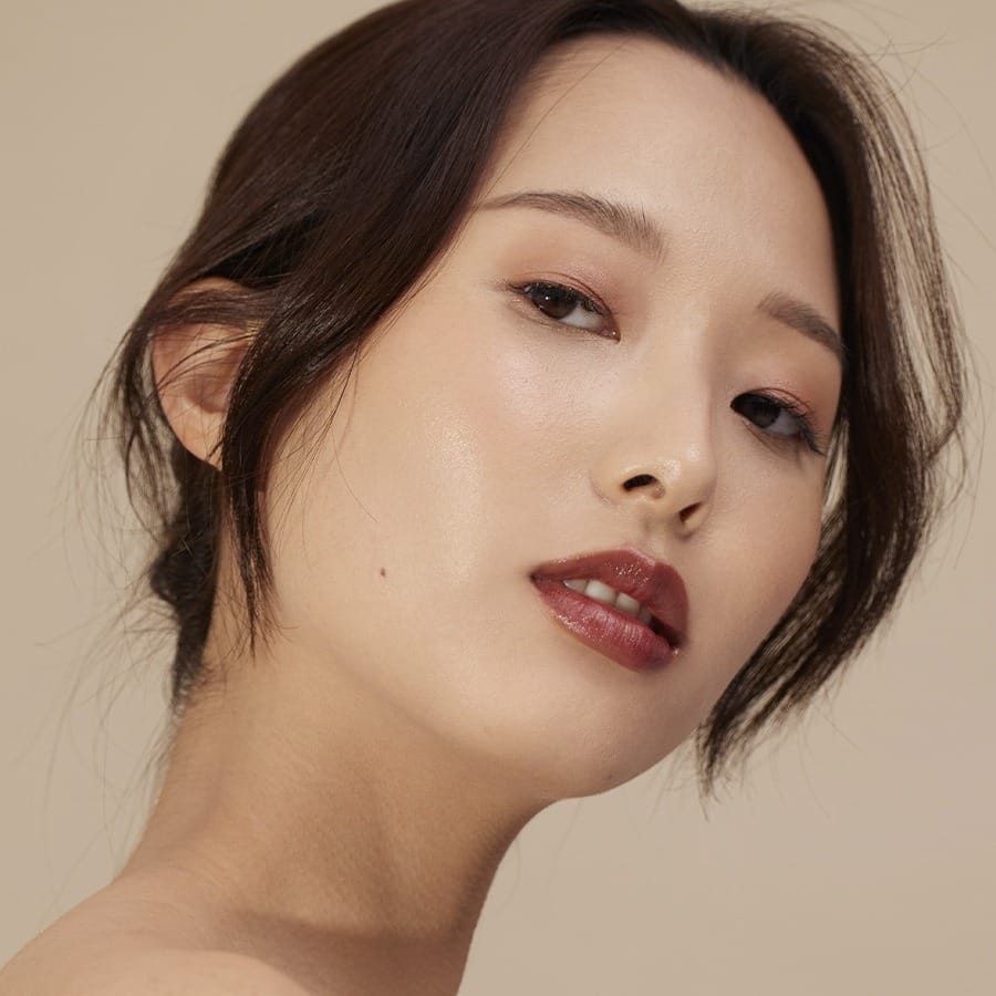 Model wearing Henné Organics Luxury Lip Tint in Nightfall for a glossy deep berry wine lip 3