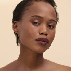 Woman with short curls and deep skin tone wearing Henné Organics Luxury Lip Tint in Nightfall 5