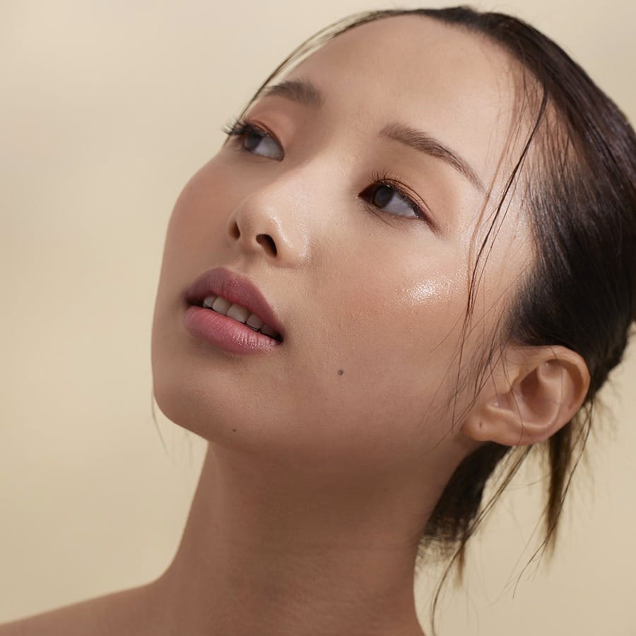 Model looking up wearing Henné Organics Luxury Lip Tint in Sunlit for a soft rosy nude lip 4