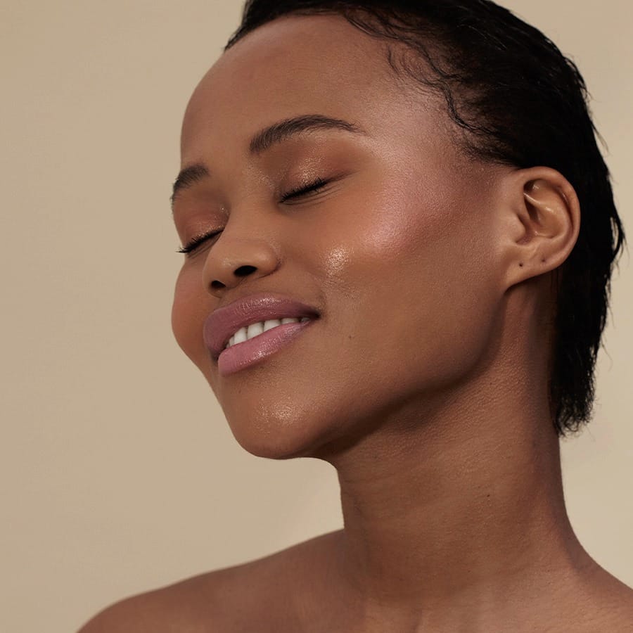 Woman with short curls and eyes closed wearing Henné Organics Luxury Lip Tint in Sunlit for a sheer pink lip 3