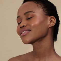 Woman with short curls and eyes closed wearing Henné Organics Luxury Lip Tint in Sunlit for a sheer pink lip 3