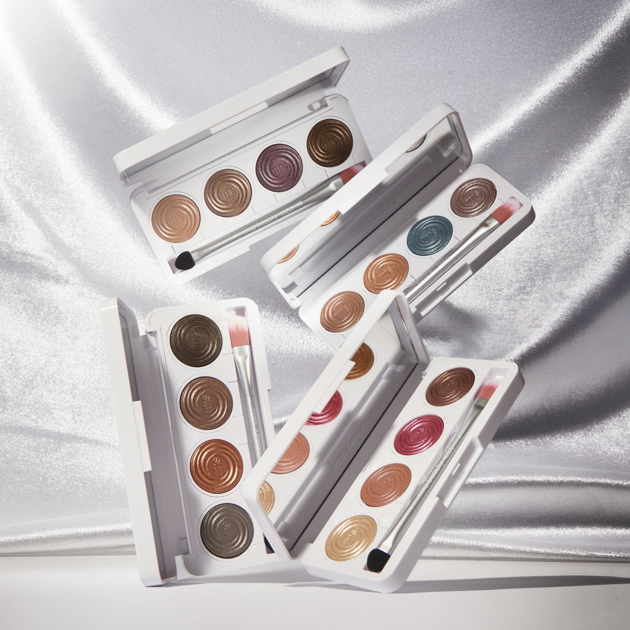 Four Hydra Eyes Quartet eyeshadow palettes open and styled together on satin fabric 7