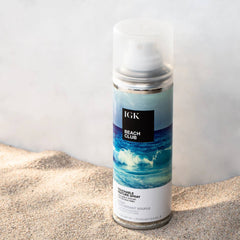 IGK Beach Club Touchable Texture Spray 5 oz can with ocean wave label standing in beach sand