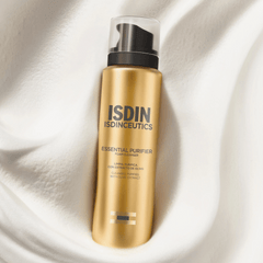 Gold bottle of ISDIN Isdinceutics Essential Purifier on a white fabric background
