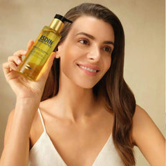 Woman with glowing skin holding ISDIN Isdinceutics Essential Cleansing oil-based cleanser bottle