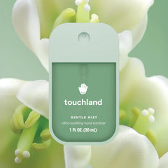 Touchland Gentle Mist Lily of the Valley hand sanitizer in front of creamy white blossoms on sage green