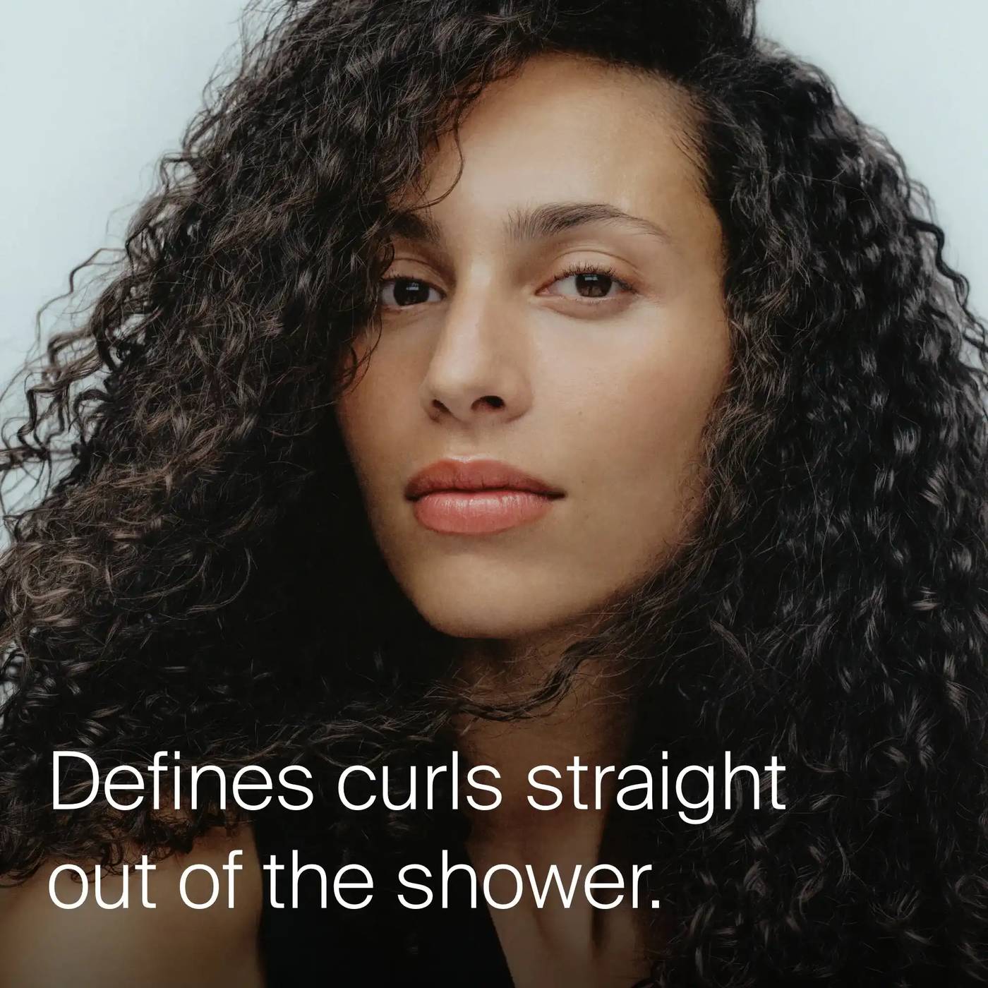 Woman with long defined dark curls showing Living Proof Curl Conditioner defining curls straight out of the shower