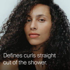 Woman with long defined dark curls showing Living Proof Curl Conditioner defining curls straight out of the shower