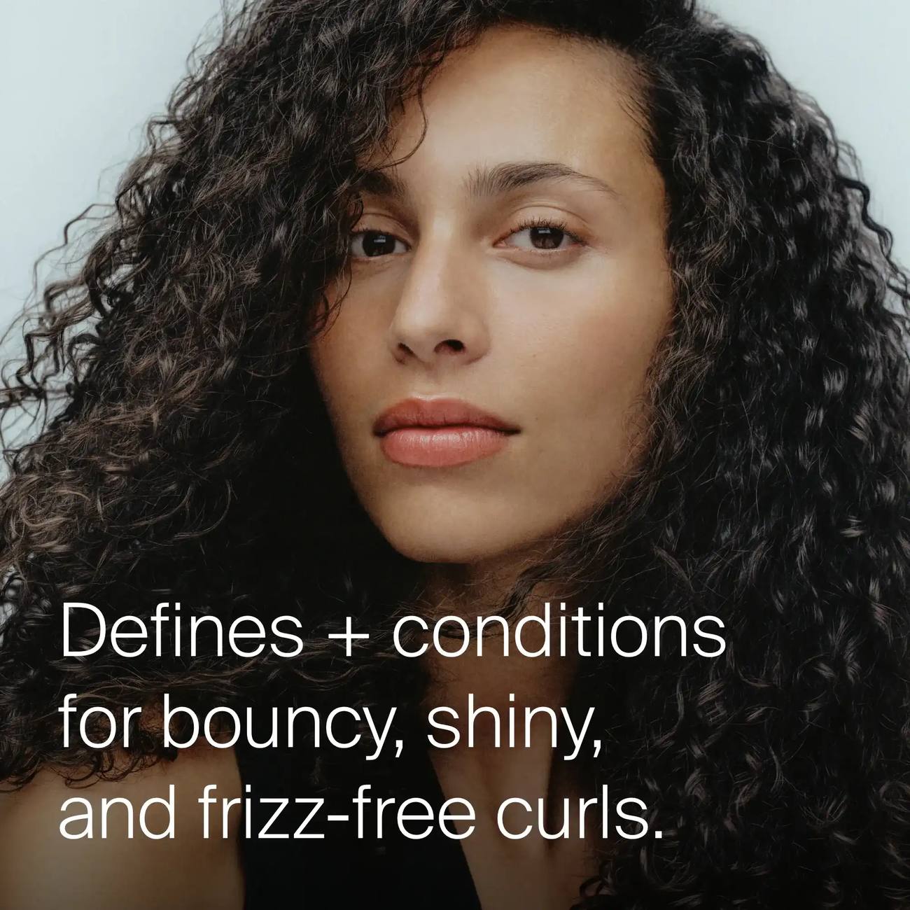Woman with long dark curls showing Living Proof Curl Definer for bouncy shiny frizz free curls