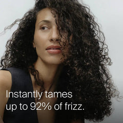 Woman with long dark curls showing Living Proof No Frizz Instant De-Frizzer taming up to 92 percent of frizz