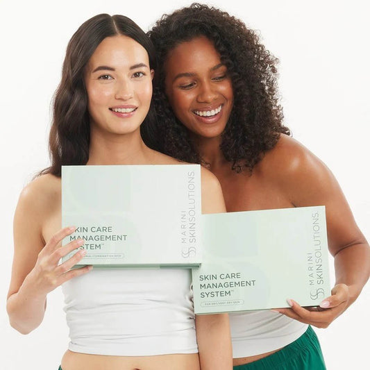Two women holding Marini Skin Solutions Skin Care Management System boxes for normal/combination and dry/very dry skin 2