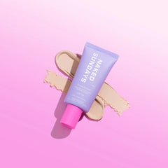 Naked Sundays BeautyBarrier SPF50 priming lotion tube resting on cream lotion swatches on a pink background