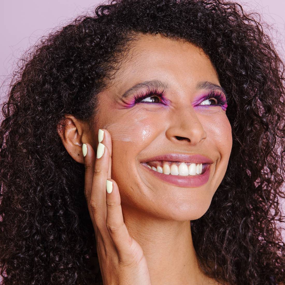 Smiling woman with colorful eye makeup applying Naked Sundays CabanaClear illuminating water gel serum SPF50