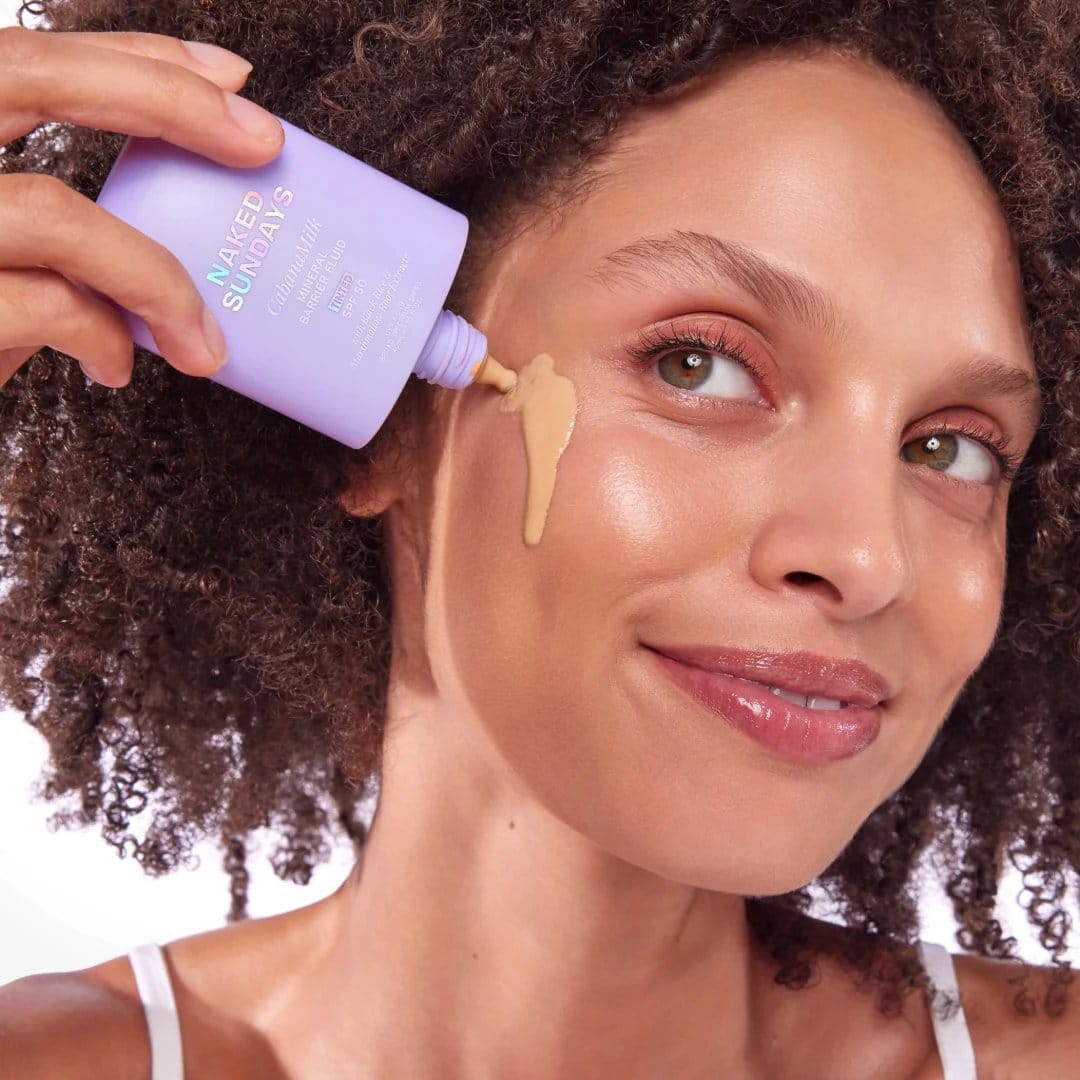 Woman applying Naked Sundays CabanaMilk SPF50 mineral barrier fluid under her eye
