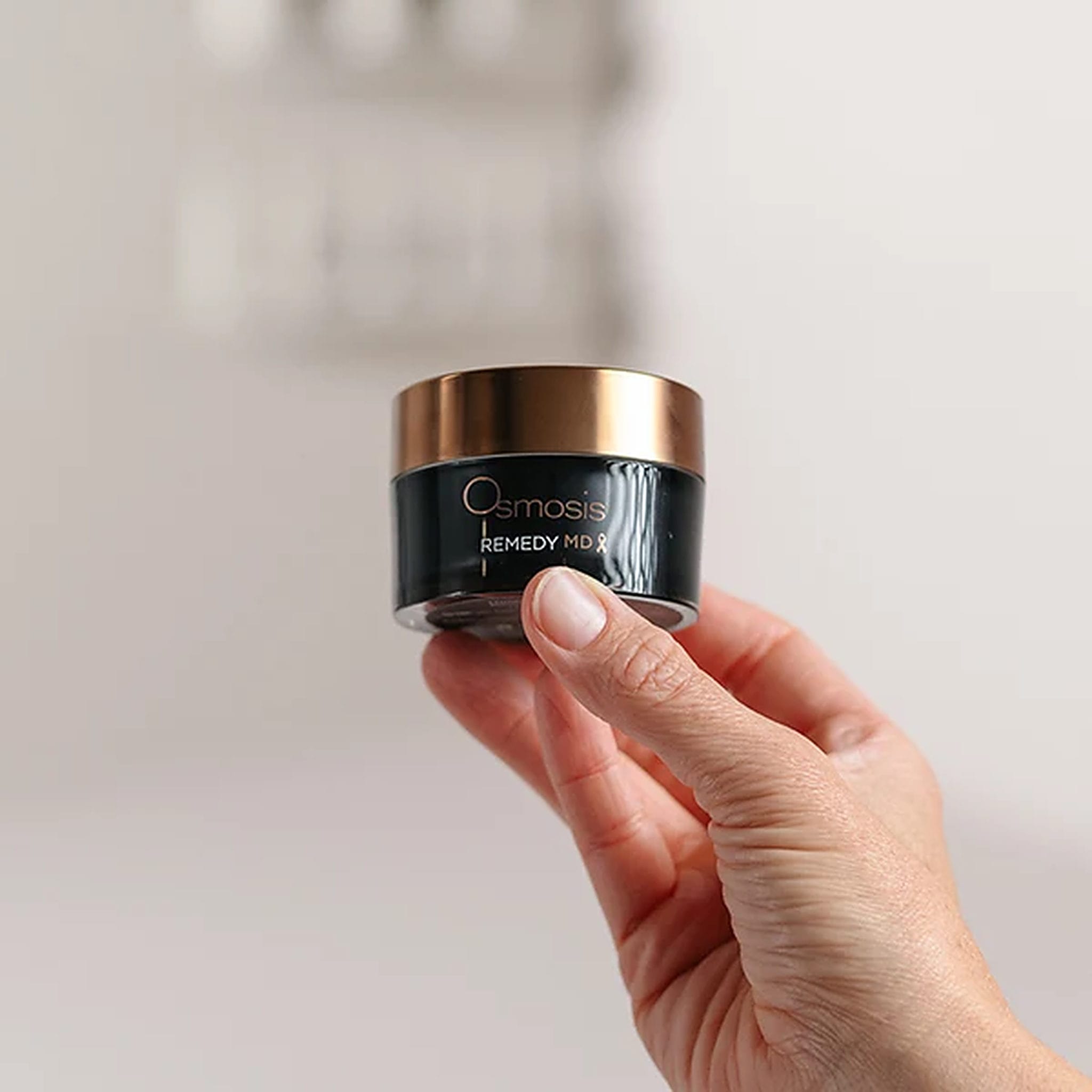 Hand holding Osmosis Remedy MD healing balm jar to show compact size