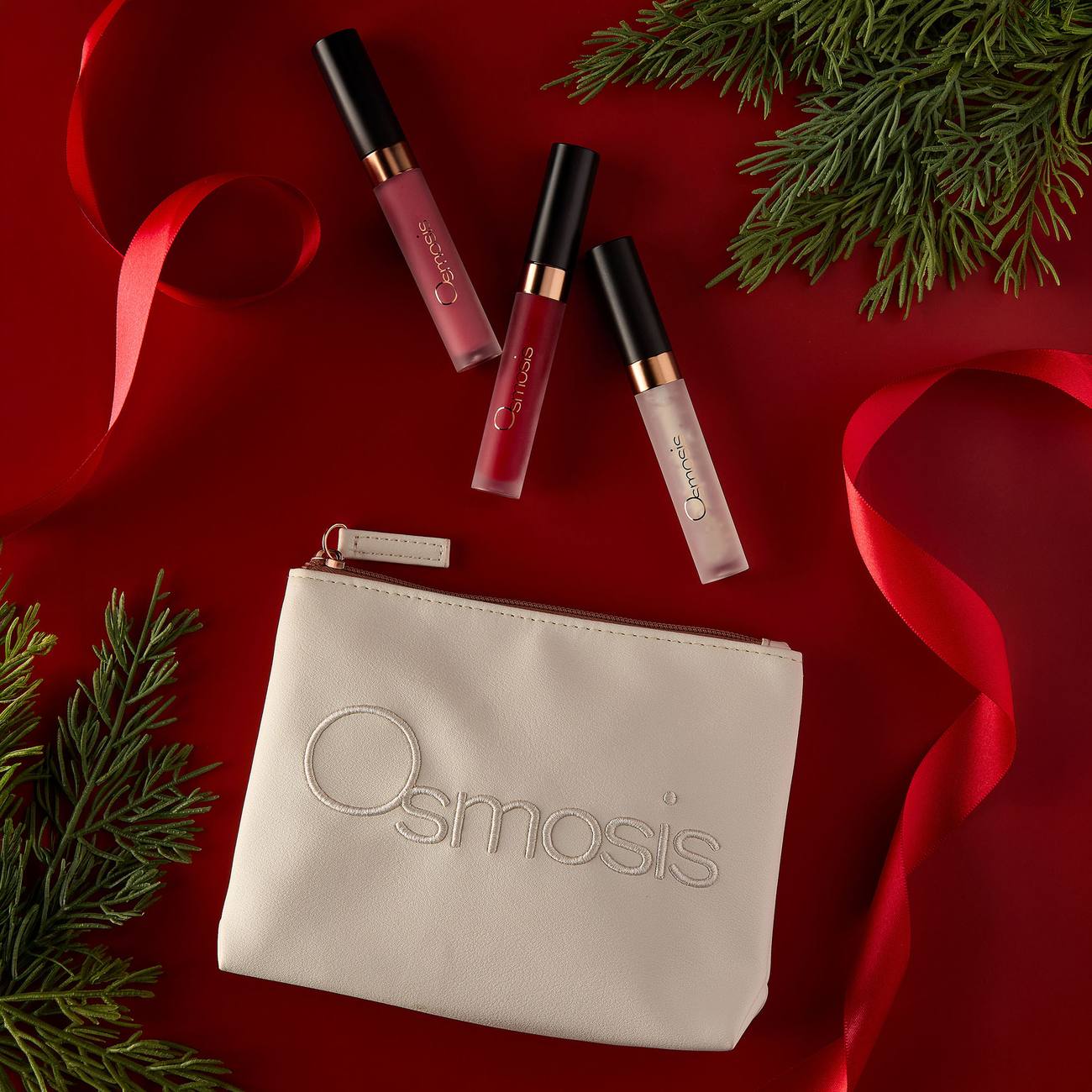 Osmosis Under the Mistletoe Lip Kit styled on a red background with pine branches and ribbon