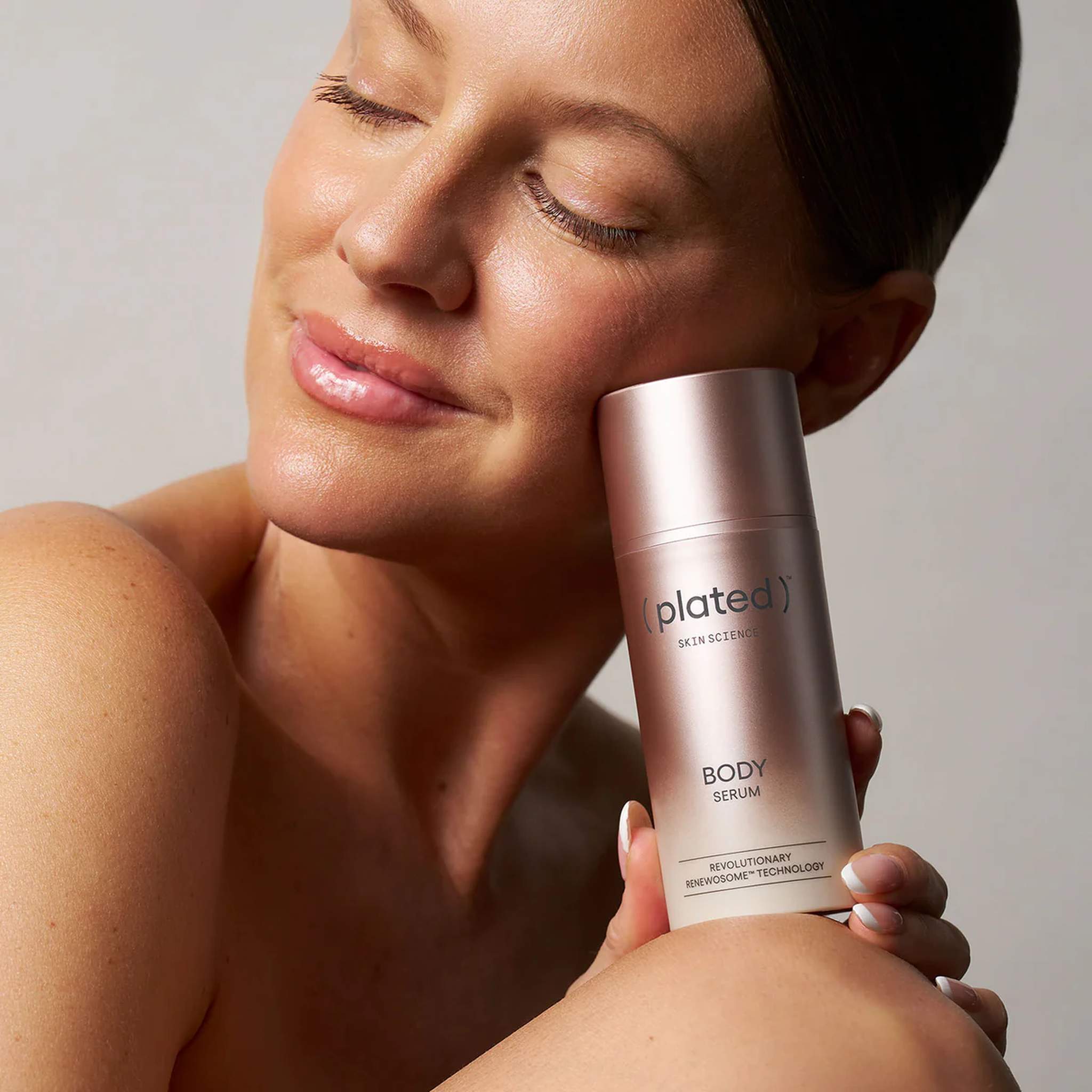 Woman resting Plated Body Serum against her cheek to highlight body and face skincare