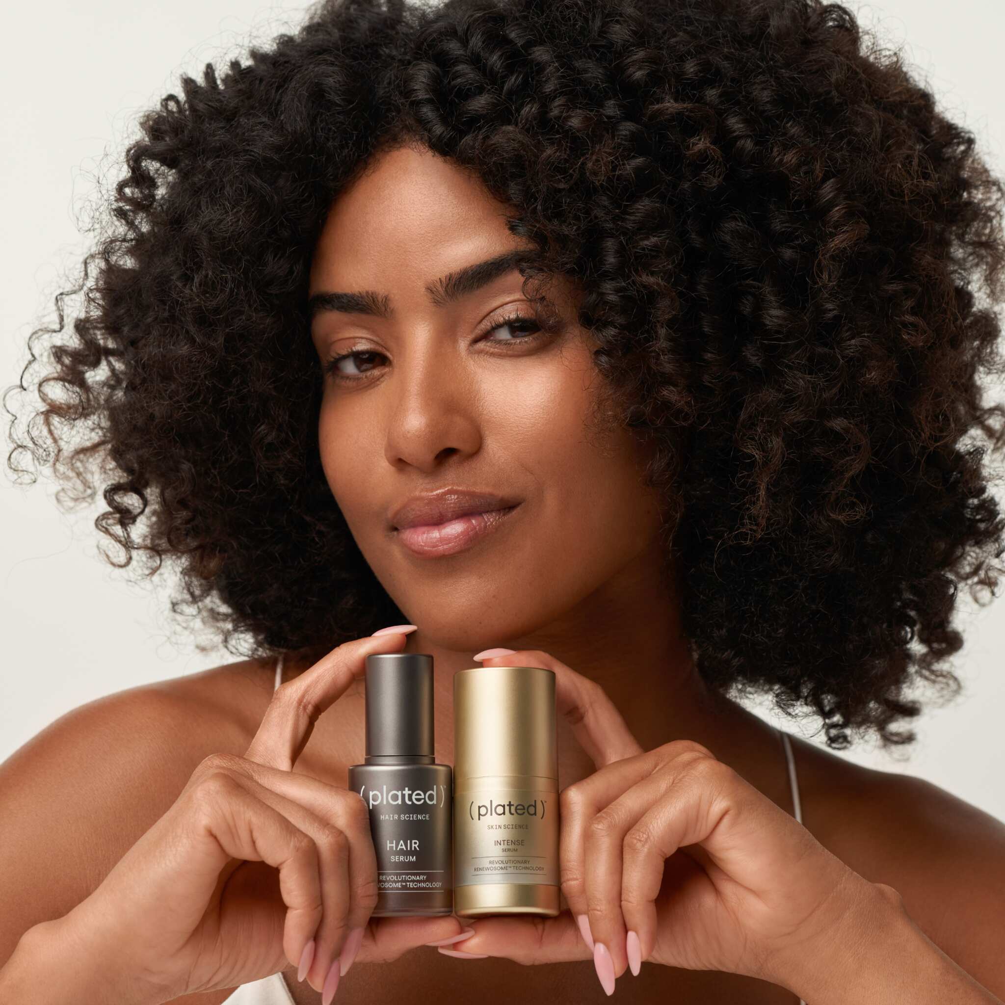 Woman with curly hair holding Plated Hair Serum and Intense Serum