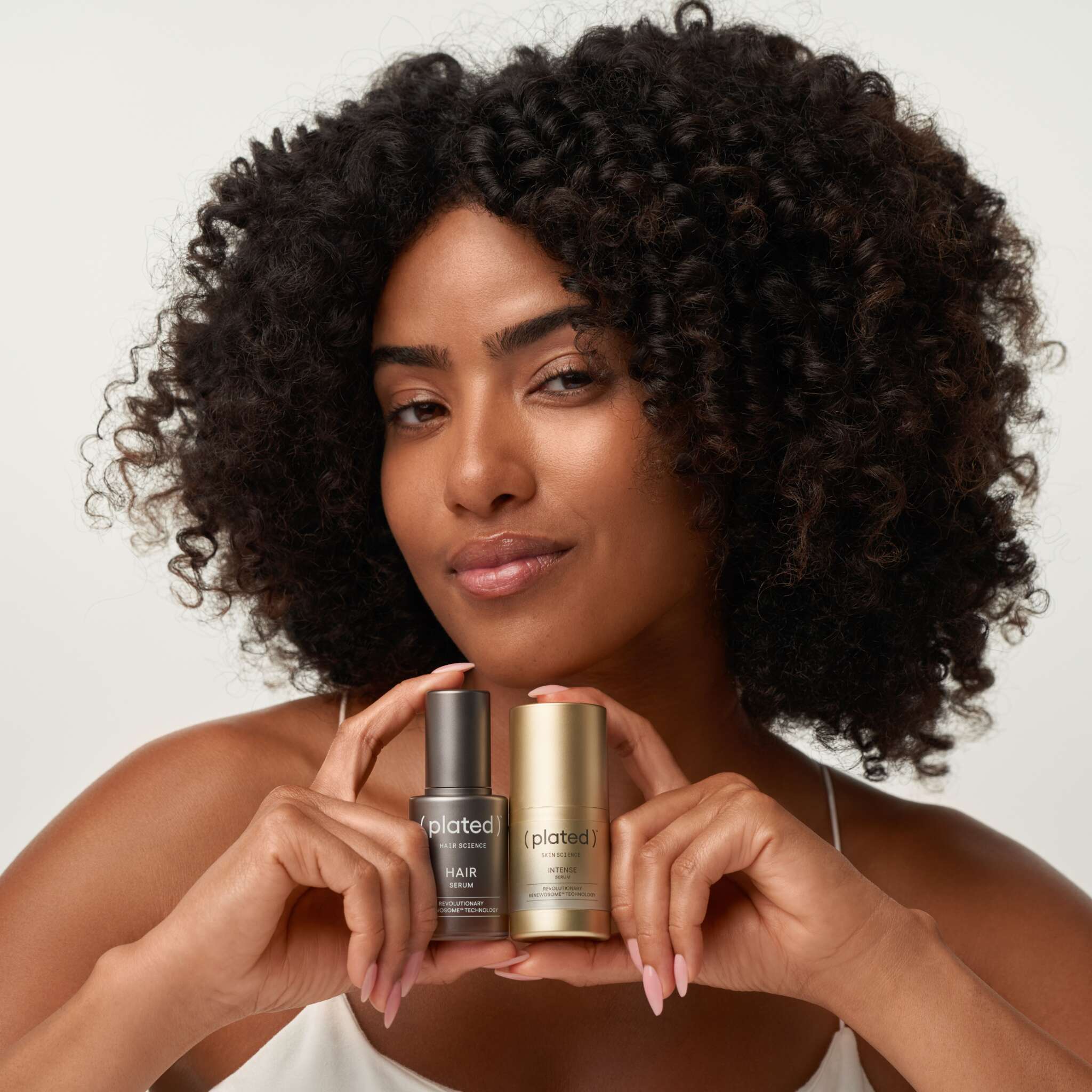 Woman with curly hair holding Plated Hair Serum and Intense Serum