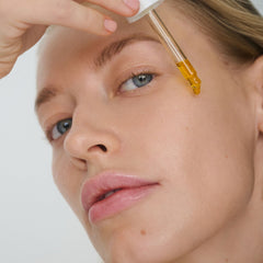 Model applying Kakadu Beauty Oil to forehead with glass dropper