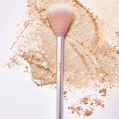 RMS Beauty Skin2Skin highlighter brush resting on swirled golden powder
