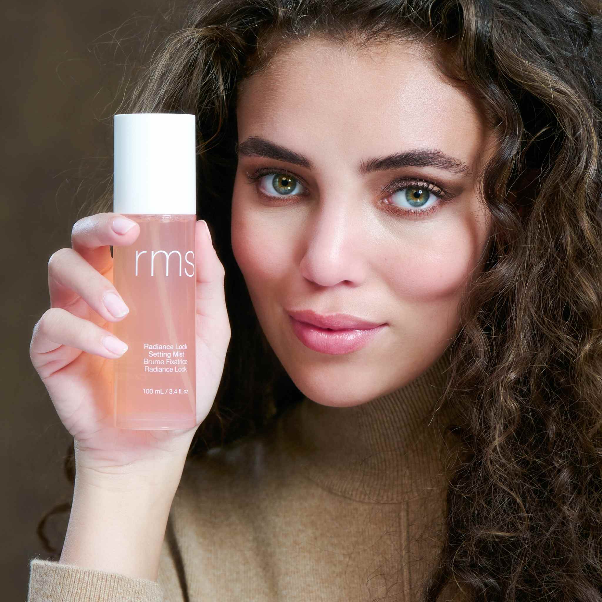 Model holding RMS Beauty Radiance Lock Setting Mist bottle near her face