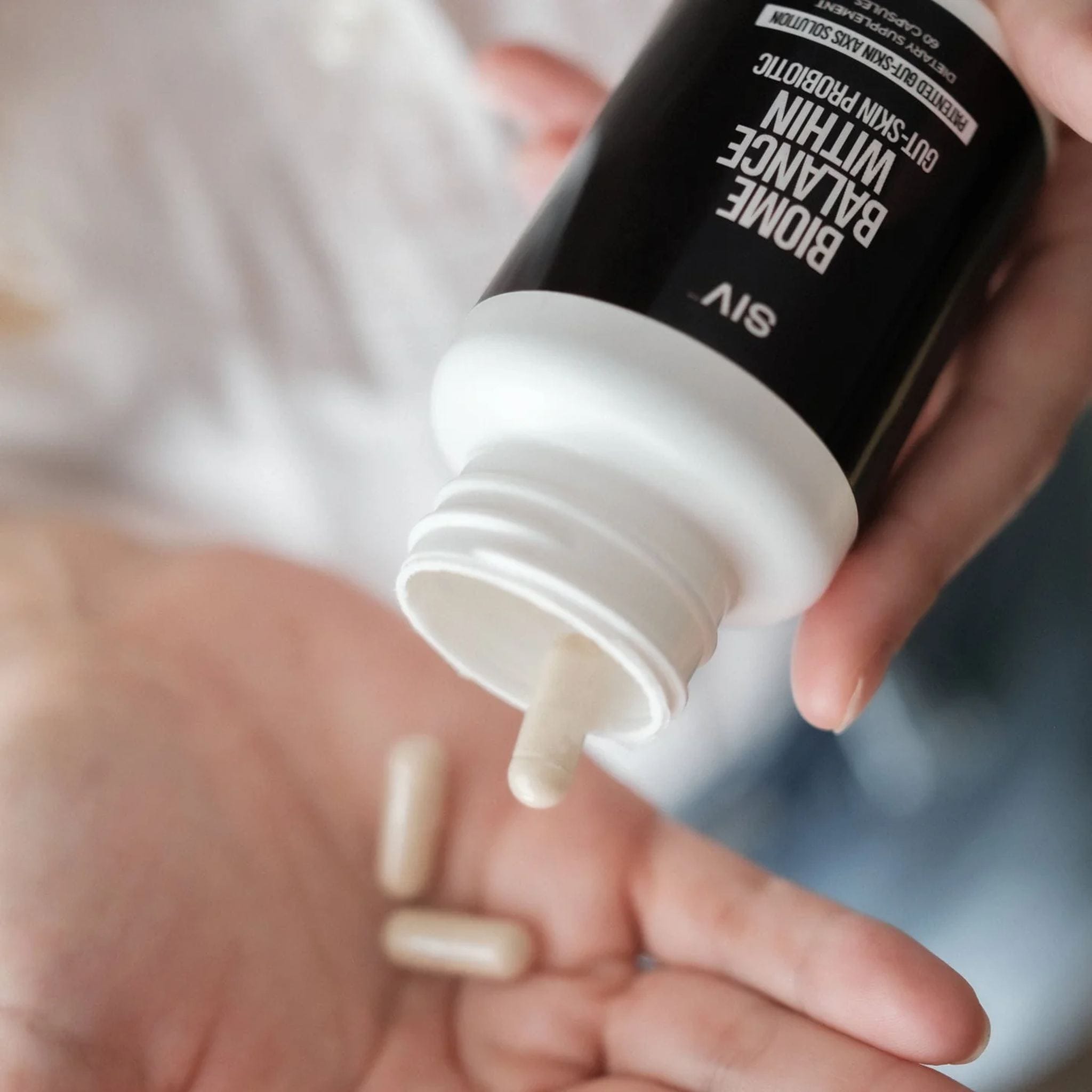 Hand pouring SIV Biome Balance Within probiotic capsules from bottle