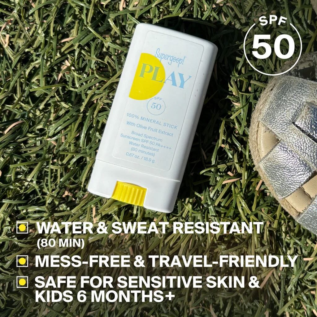 PLAY Mineral Stick SPF 50 resting on grass next to a sandal for travel-friendly sun care
