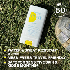 PLAY Mineral Stick SPF 50 resting on grass next to a sandal for travel-friendly sun care