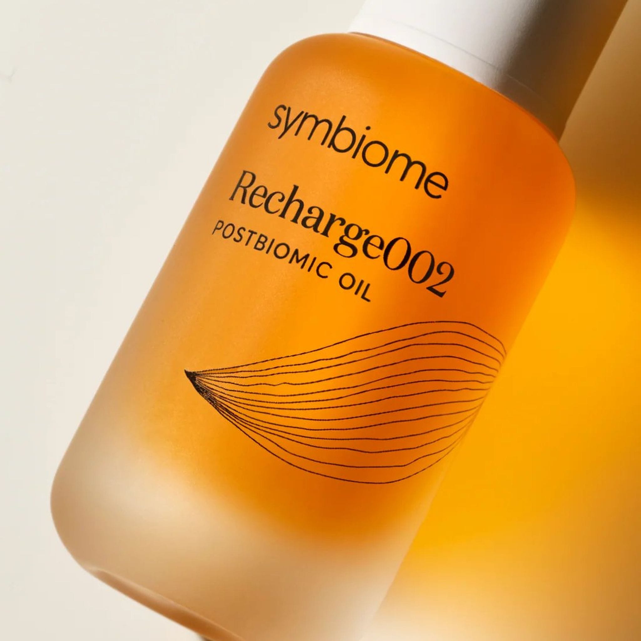 Close-up of Symbiome Recharge002 Postbiomic Oil amber bottle label showing brand name and botanical line art detail