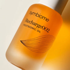 Close-up of Symbiome Recharge002 Postbiomic Oil amber bottle label showing brand name and botanical line art detail