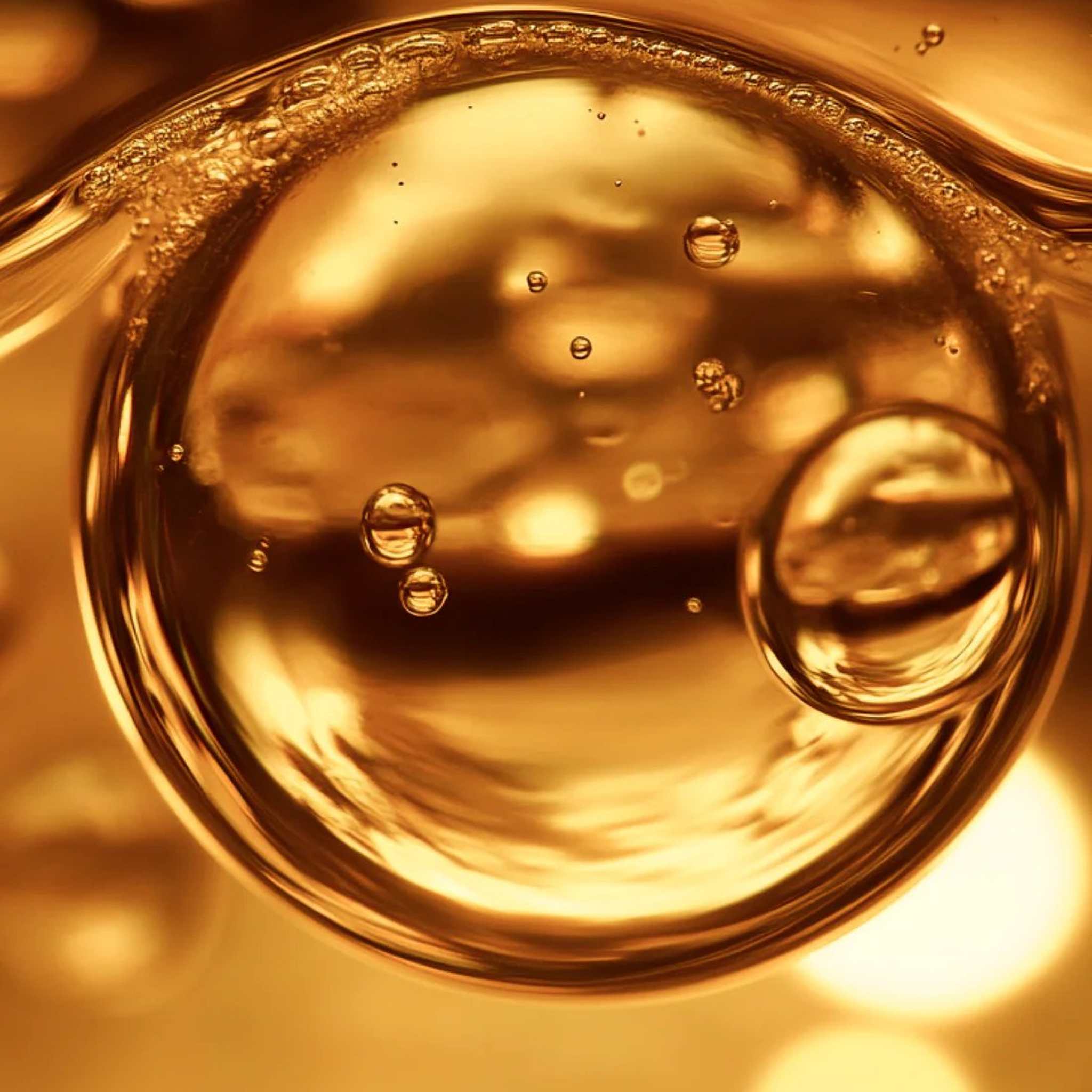 Macro close-up of golden oil droplets and bubbles showing the rich luxurious texture of Symbiome Recharge002 Postbiomic Oil