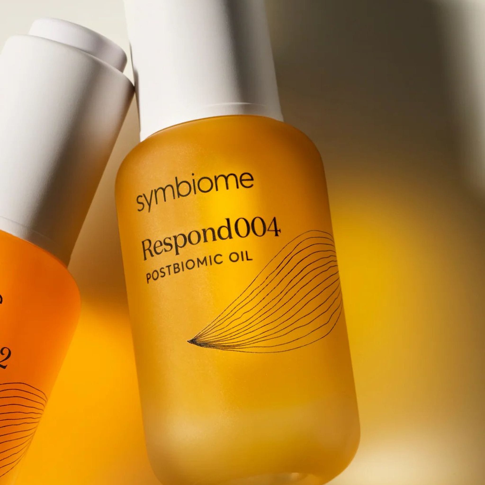 Close-up of two Symbiome Respond004 and Recharge002 Postbiomic Oil bottles showing label detail and amber glass