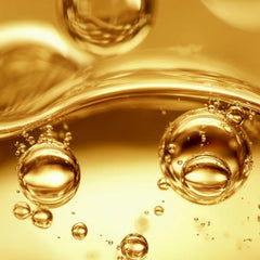 Macro close-up of golden oil droplets and reflective bubbles showing the luxurious texture of Symbiome Respond004 Postbiomic Oil