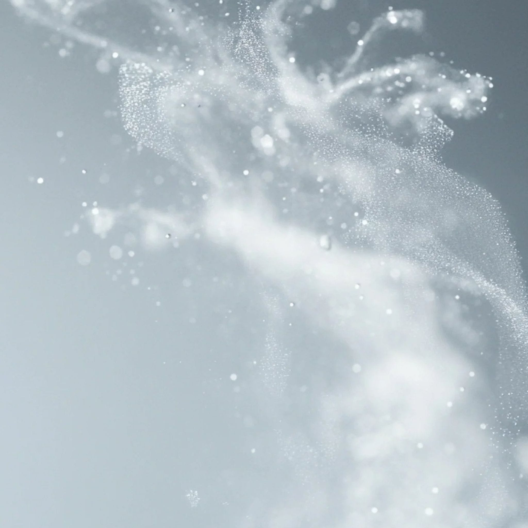 Fine mist spray burst on soft gray background showing the lightweight rejuvenating texture of Symbiome The Essence