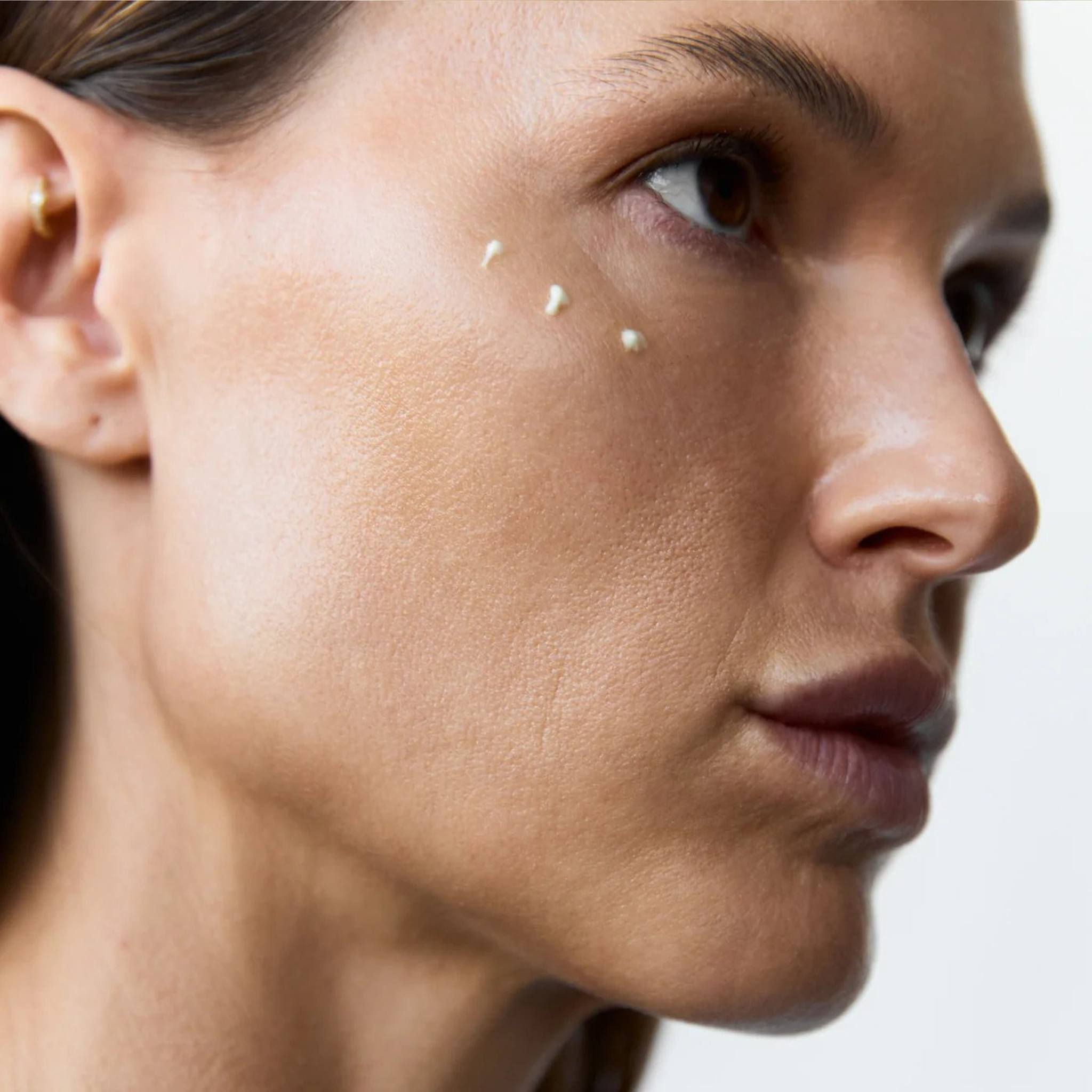 Woman with glowing skin showing small dots of Symbiome The Luminary eye cream applied under the eye area