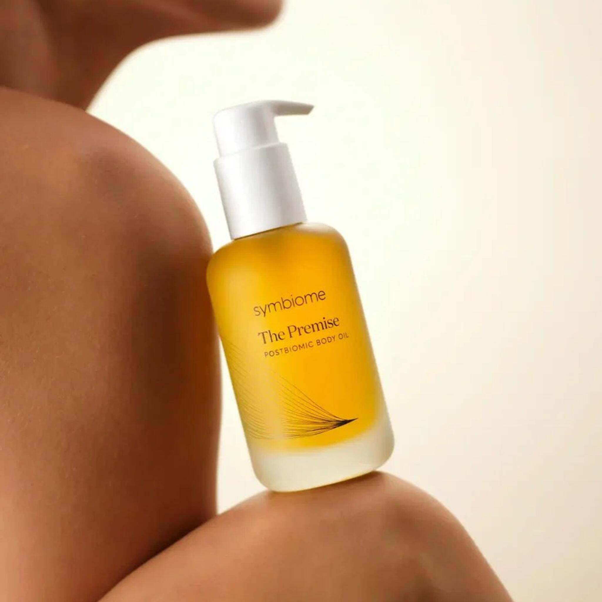 Model holding Symbiome The Premise Postbiomic Body Oil pump bottle against bare shoulder
