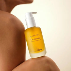 Model holding Symbiome The Premise Postbiomic Body Oil pump bottle against bare shoulder
