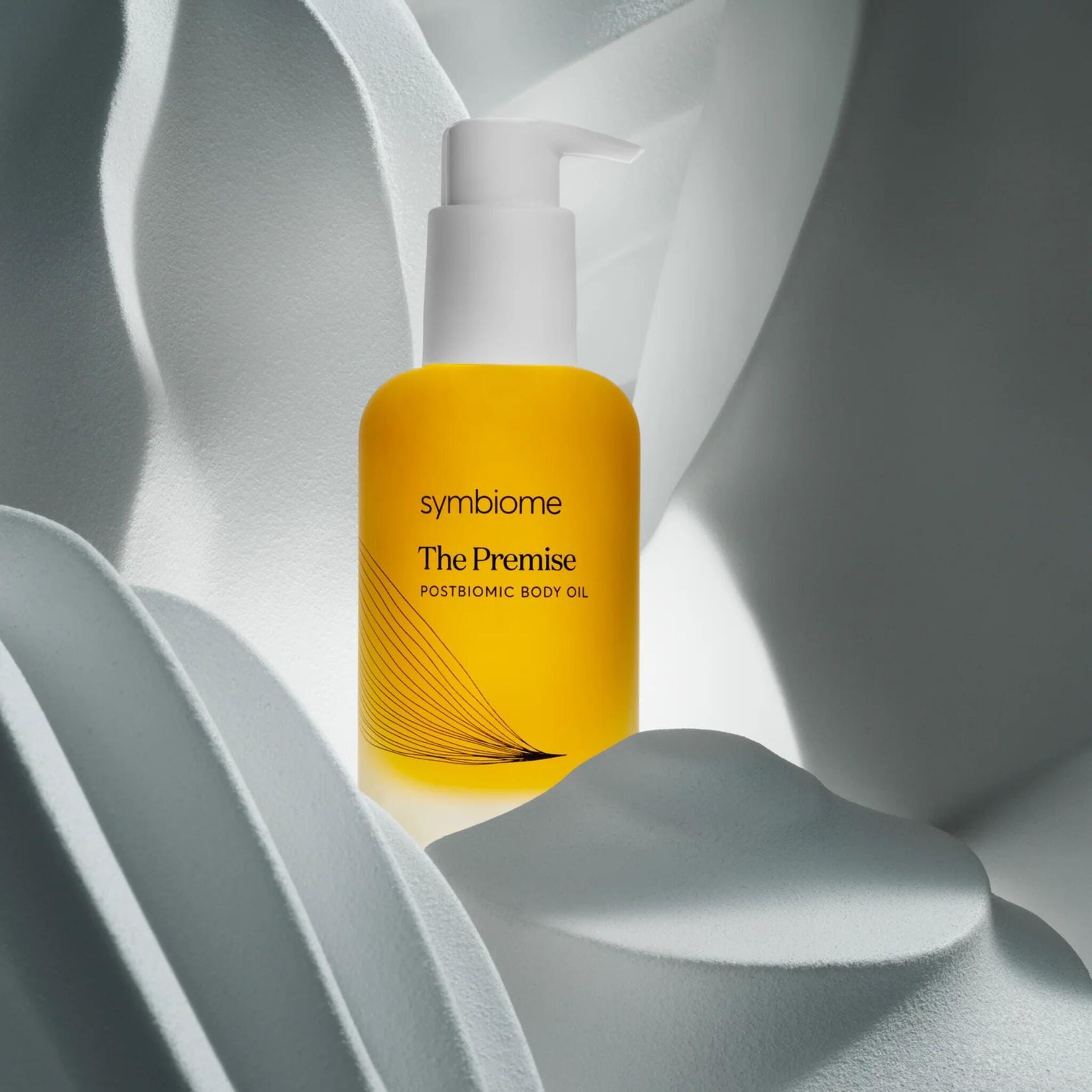 Symbiome The Premise Postbiomic Body Oil amber pump bottle nestled among sculptural white organic forms