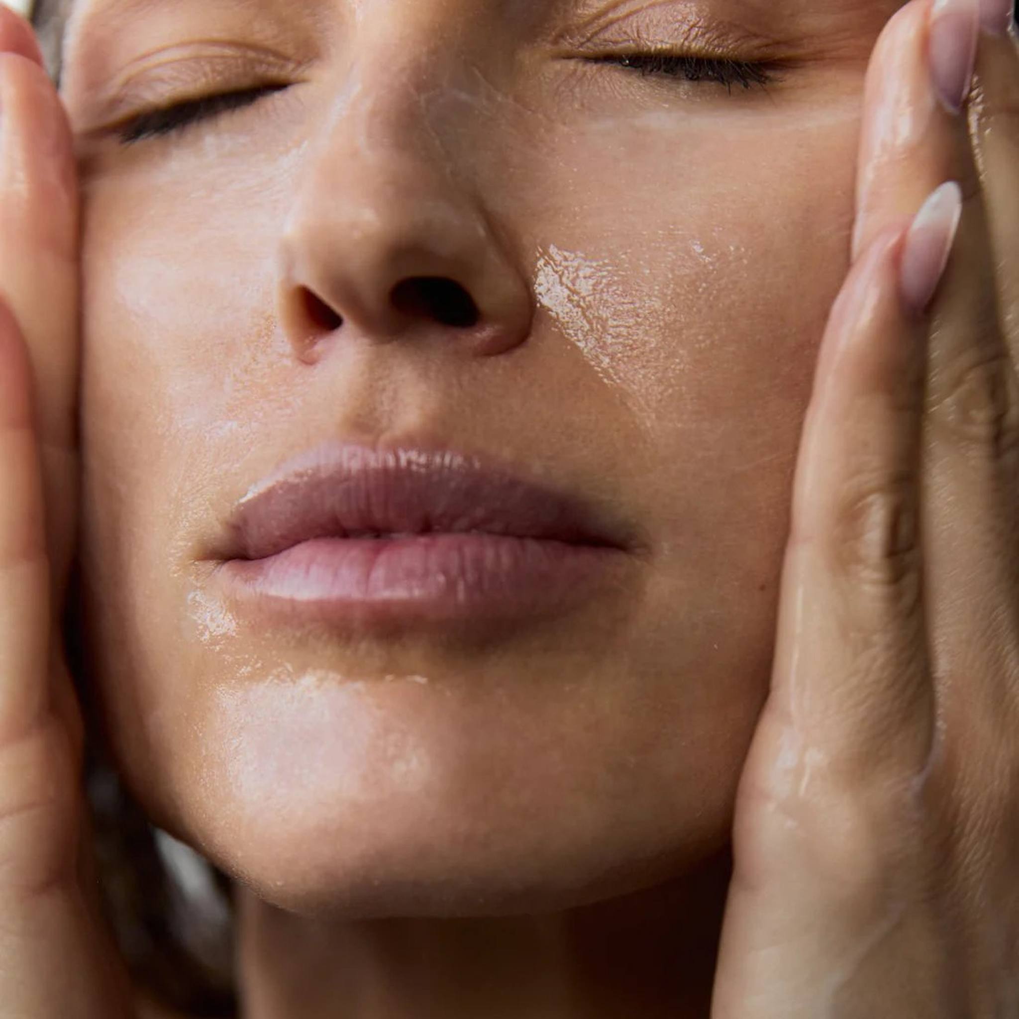 Woman massaging Symbiome The Renewal Daily Cleanser onto wet face with both hands eyes closed showing cleansing ritual